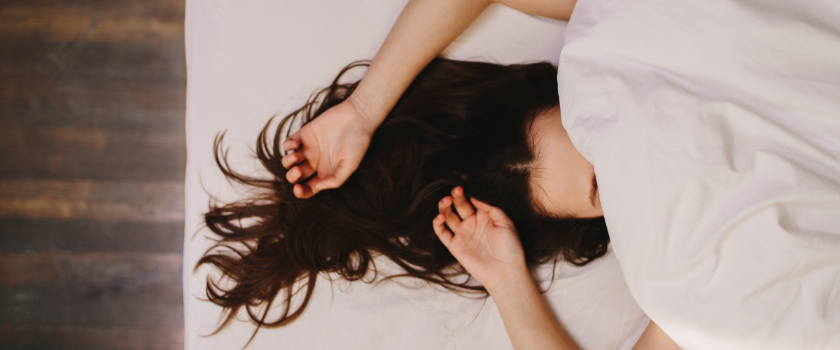 Vrouw ligt onrustig met haar armen boven haar hoofd te woelen in bed