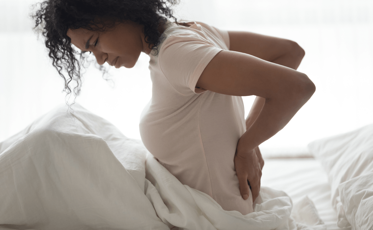 Vrouw zit rechtop in bed met haar handen op haar rug
