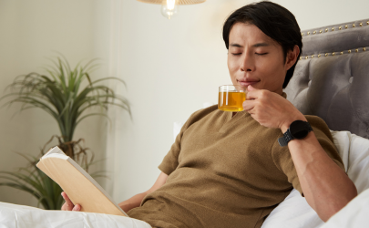 Man ligt genietend met thee in bed een boek te lezen