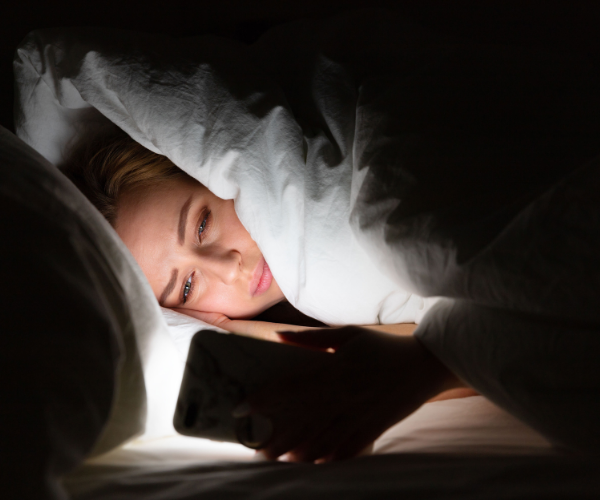 Vrouw ligt scrollend op haar mobiel in bed